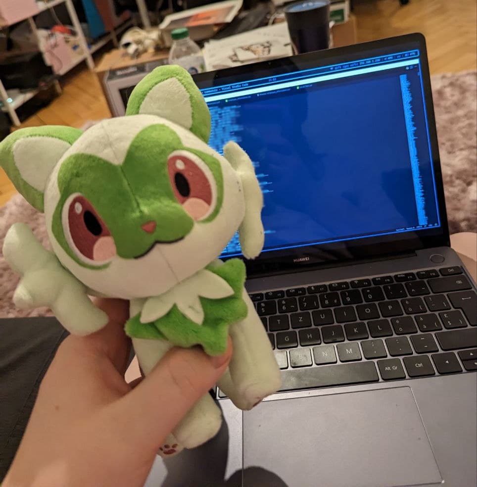 me holding a sprigatito pokemon plushie in front of a laptop screen showing a very blurry long csv list in vscode